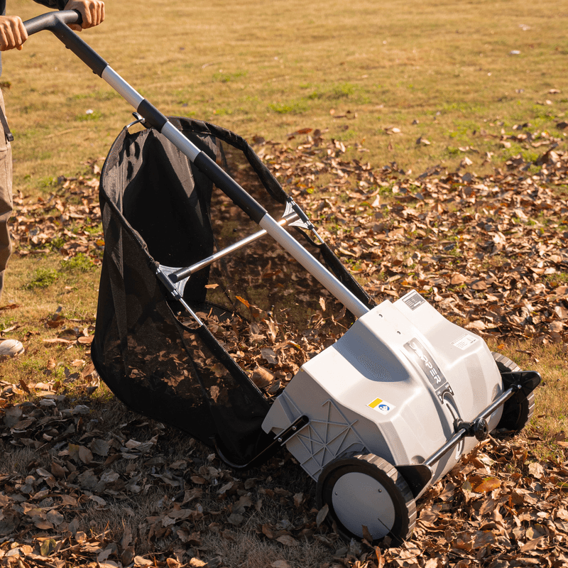 Dapper Supply push lawn sweeper collecting leaves on a lawn.