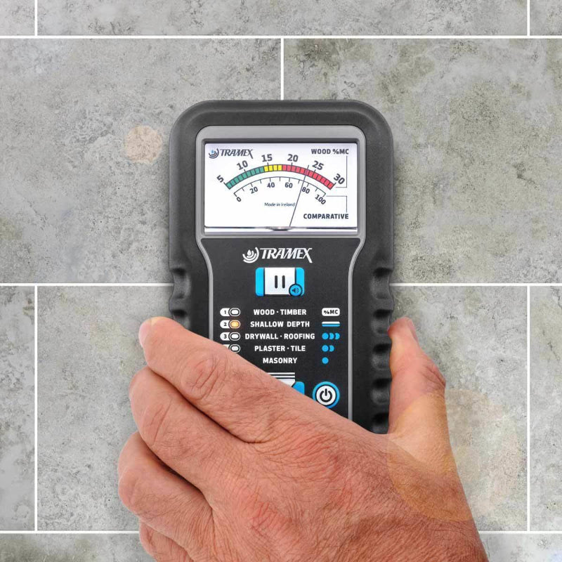 Tramex Water Damage Restoration Tech Kit - WDTK A close-up view of a Tramex ME5 moisture meter held in a hand, highlighting its ergonomic design and display against a textured gray tiled background.
