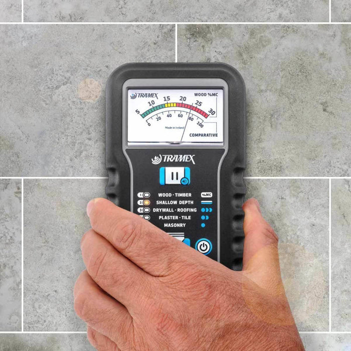 Tramex Water Damage Restoration Tech Kit - WDTK A close-up view of a Tramex ME5 moisture meter held in a hand, highlighting its ergonomic design and display against a textured gray tiled background.