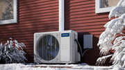 MRCOOL DIY 5th Gen condenser on a pad beside red siding in snow, line set running up the wall in a cover
