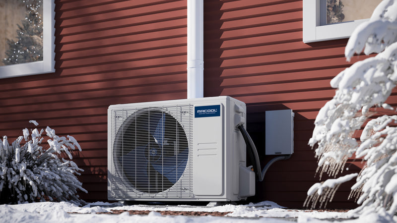 MRCOOL DIY 5th Gen condenser on a pad beside red siding in snow, line set running up the wall in a cover