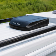 Black TravelCool mounted on a white RV roof beside a grassy field