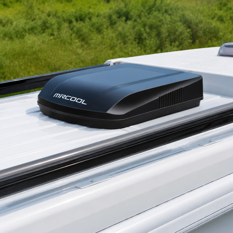 Black TravelCool mounted on a white RV roof beside a grassy field