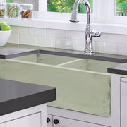 Nantucket Sinks FCFS3318D-ShabbyGreen Shabby Green double bowl farmhouse sink under a dark counter in a white kitchen