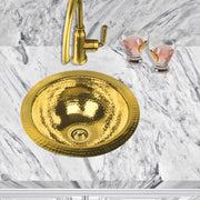 Nantucket Sinks ROB round hammered brass sink in a white marble counter with a brass faucet, top view
