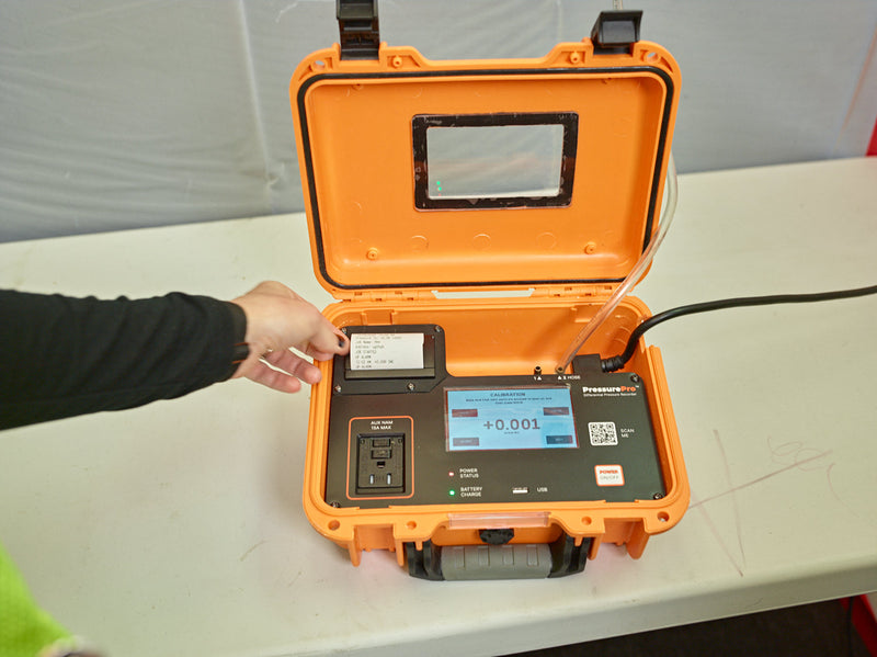 PressurePro recorder on a jobsite table, hand tearing off a printed pressure log beside the calibration screen