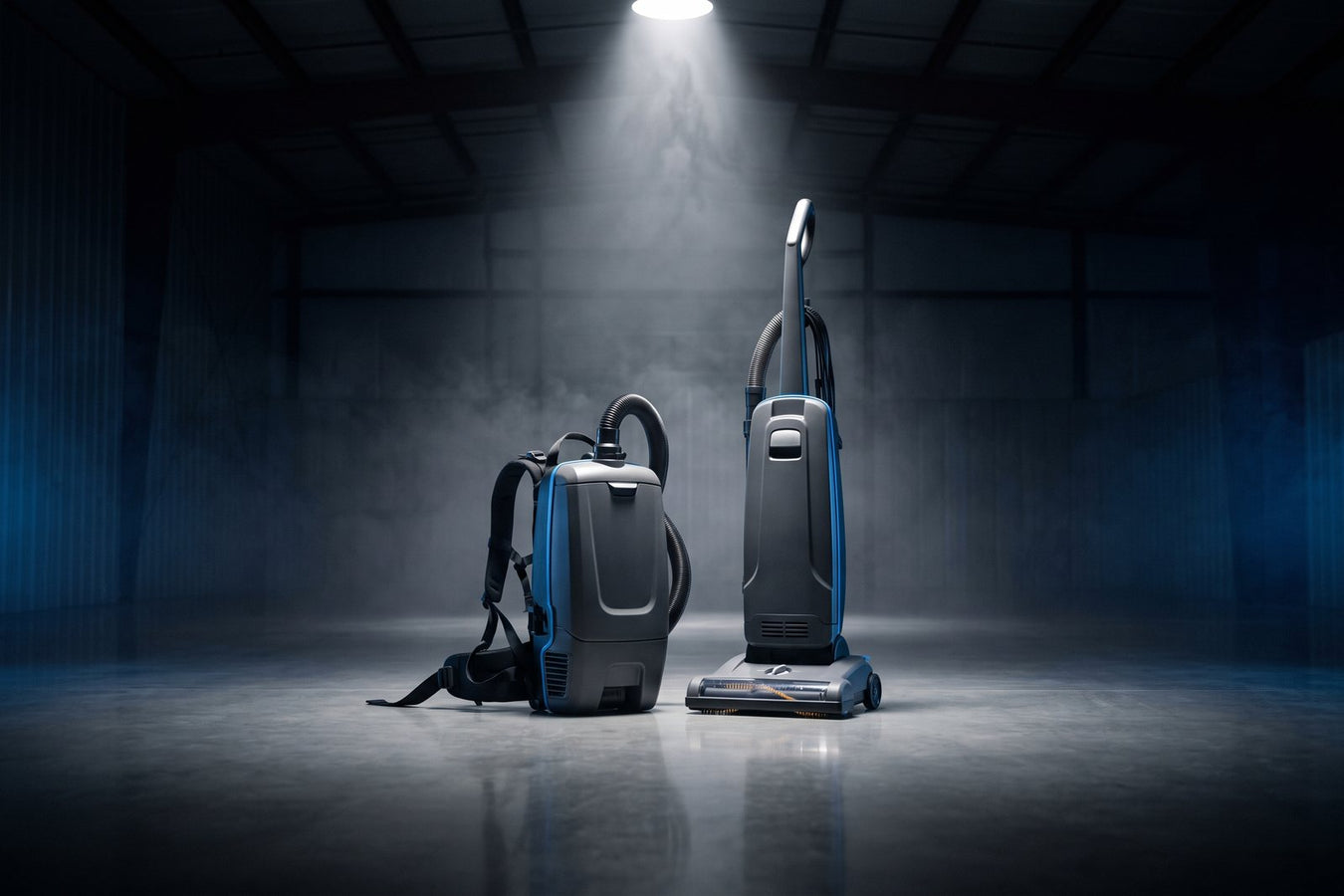 Commercial backpack vacuum and upright vacuum side by side in a dark workshop