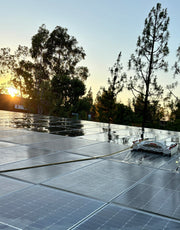 Tucker RTM solar cleaning robot on a wet rooftop solar array at sunset with its supply hose