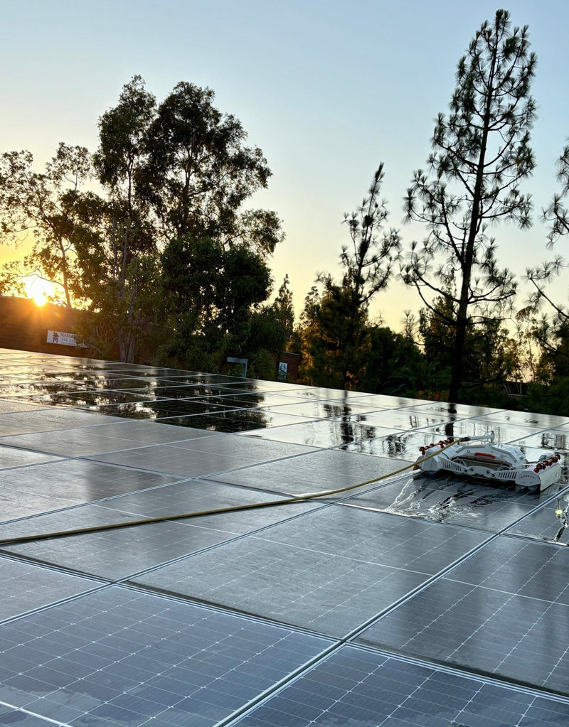 Tucker RTM solar cleaning robot on a wet rooftop solar array at sunset with its supply hose