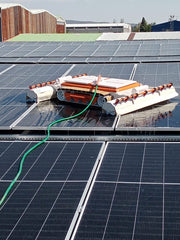 Tucker RTM solar cleaning robot washing rooftop solar panels fed by a green water hose