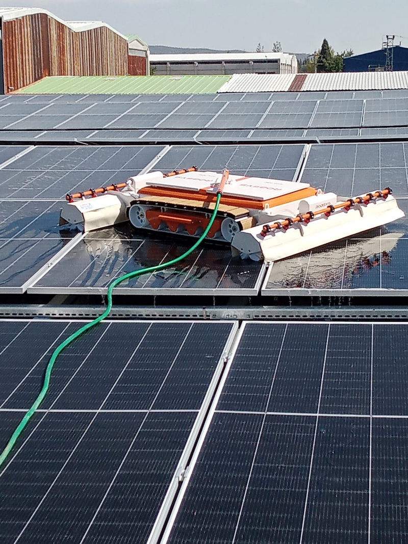 Tucker RTM solar cleaning robot washing rooftop solar panels fed by a green water hose